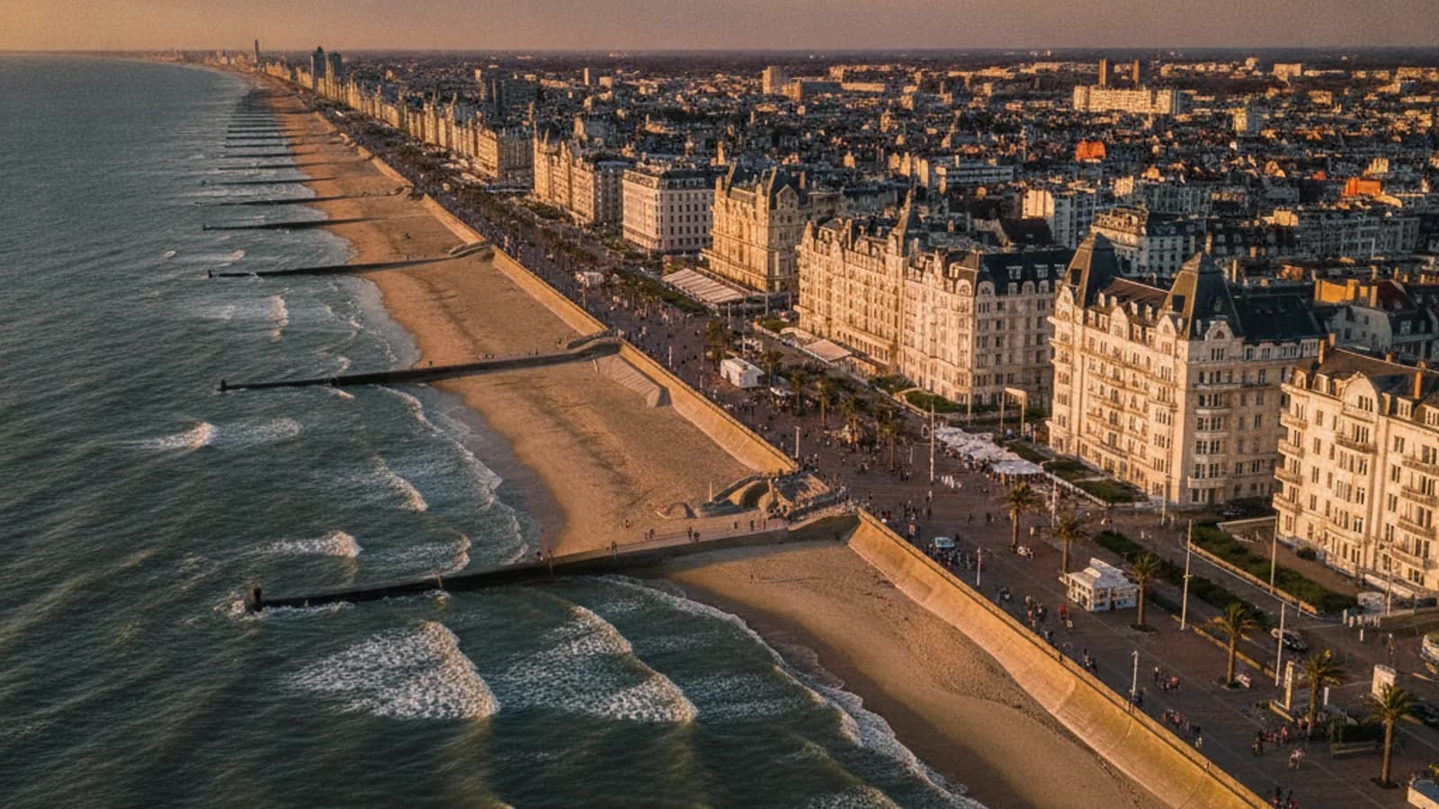 Vue aérienne du front de mer d'Ostende, avec la plage, les digues, et les bâtiments élégants bordant la côte, sous un ciel légèrement nuageux.