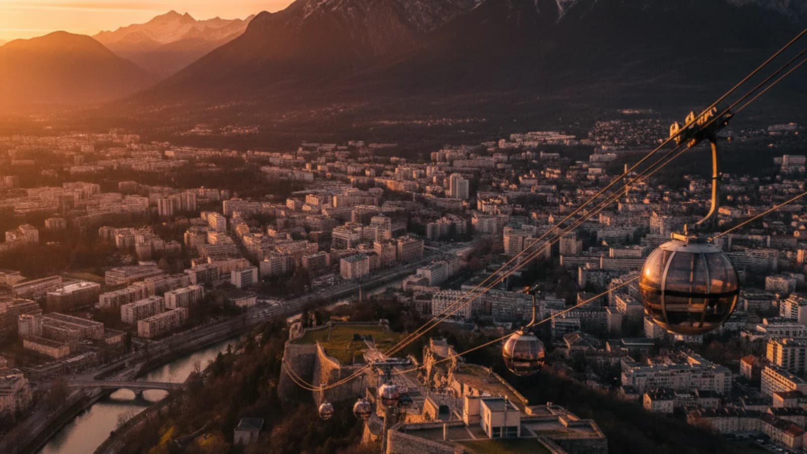Vue panoramique de Grenoble avec le téléphérique des 'bulles' montant vers la Bastille, dominée par les montagnes majestueuses
