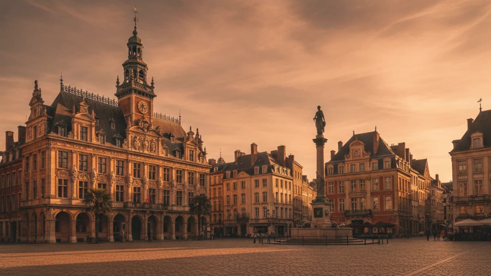 Vue panoramique de la Grand-Place de Lille un jour ensoleillé, avec la Vieille Bourse et le beffroi de la Chambre de Commerce en arrière-plan, quelques passants et terrasses.