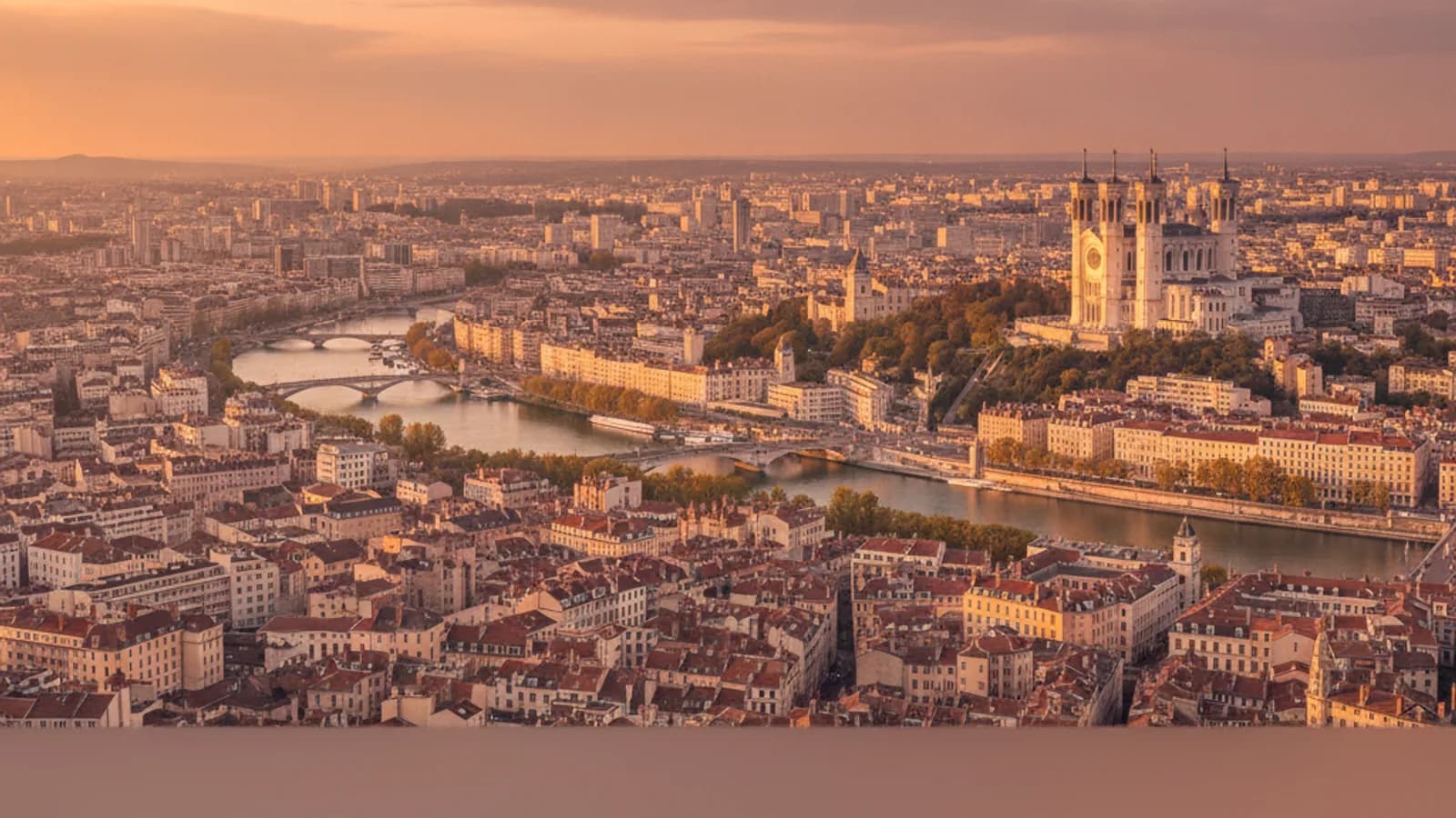 Vue panoramique sur Lyon au coucher du soleil, avec la basilique de Fourvière illuminée dominant la ville et la Saône en contrebas.