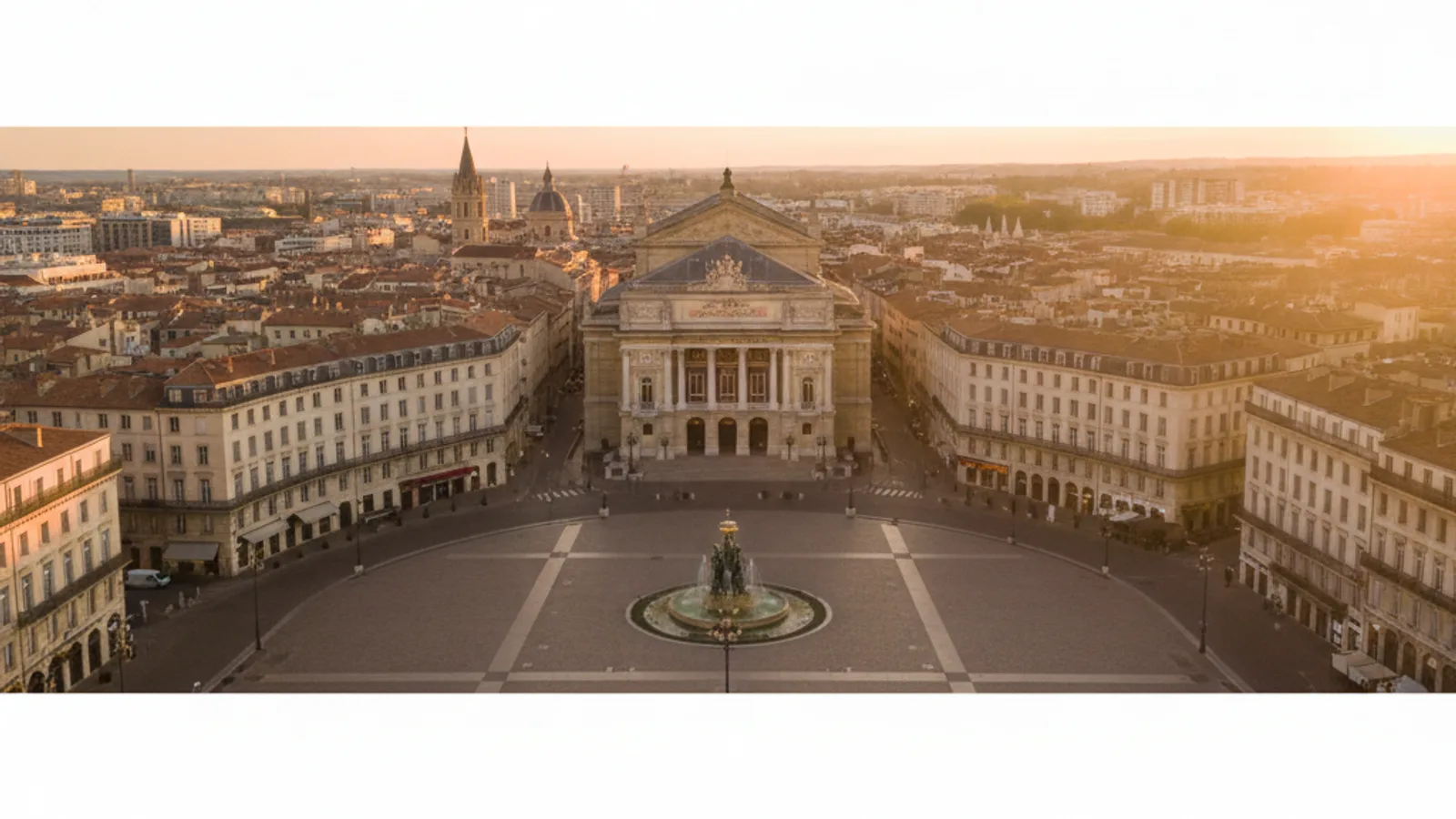 Vue aérienne de la Place de la Comédie à Montpellier, avec l'Opéra Comédie et la fontaine des Trois Grâces, sous un ciel bleu.
