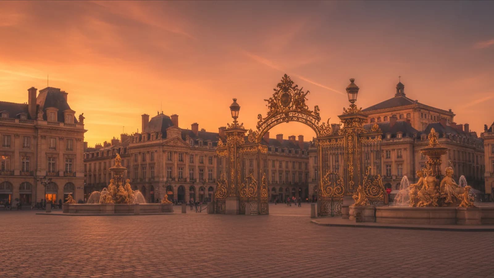 Vue aérienne de la Place Stanislas à Nancy avec ses grilles dorées et la fontaine de Neptune, entourée de bâtiments historiques sous un ciel clair.