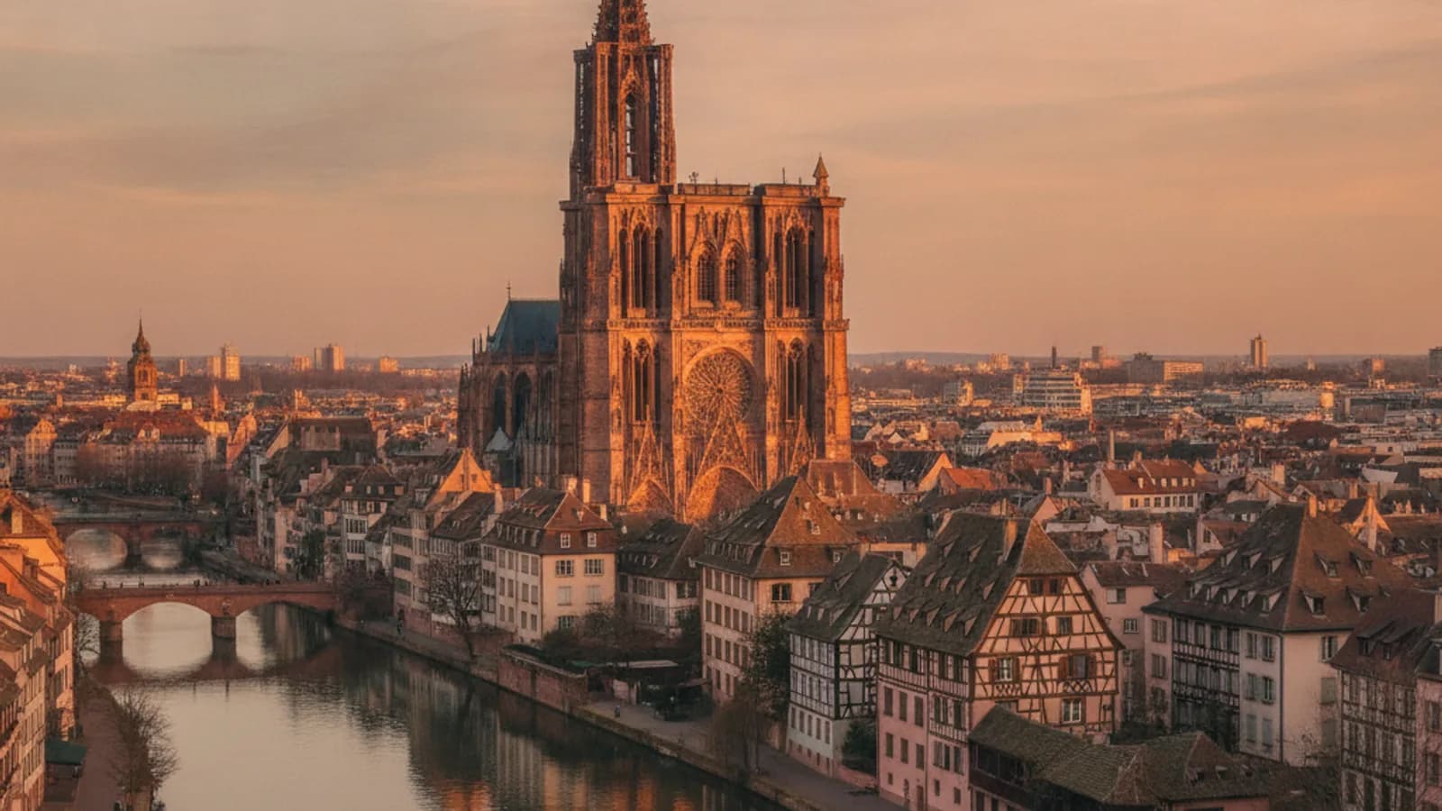 Vue aérienne des toits de la Petite France à Strasbourg, avec la Cathédrale Notre-Dame en arrière-plan et l'Ill serpentant entre les maisons à colombages.